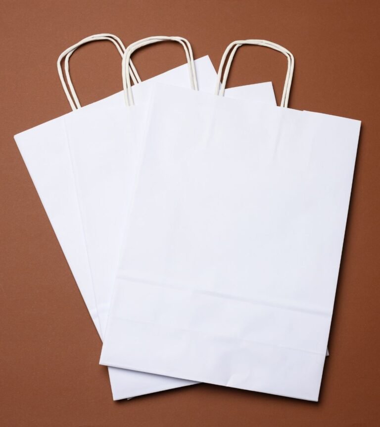 Three white paper shopping bags with matching twisted paper handles are fanned out against a solid brown background.